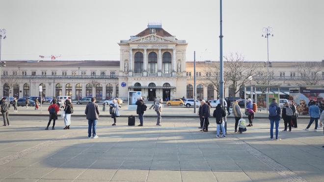Zagreb's main railway station, Glavni Kolodvor, with travelers crossing the square in front of the neoclassical facade.