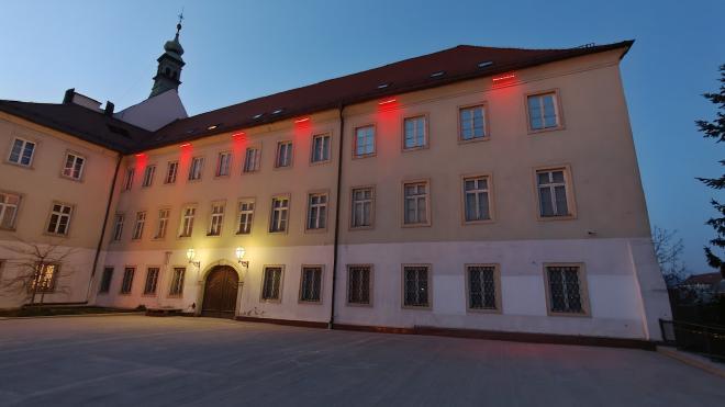 A baroque building in Zagreb at blue hour, with red accent lights along the eaves and a small bell tower above the roof.