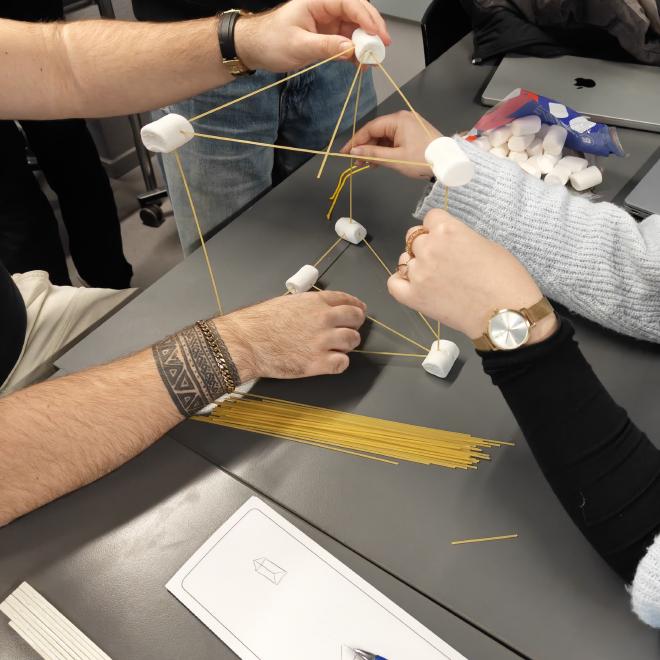 Students collaborating on a tetrahedral spaghetti-and-marshmallow structure mid-build